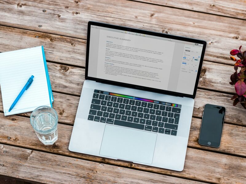 silver MacBook beside space gray iPhone 6 and clear drinking glass on brown wooden top